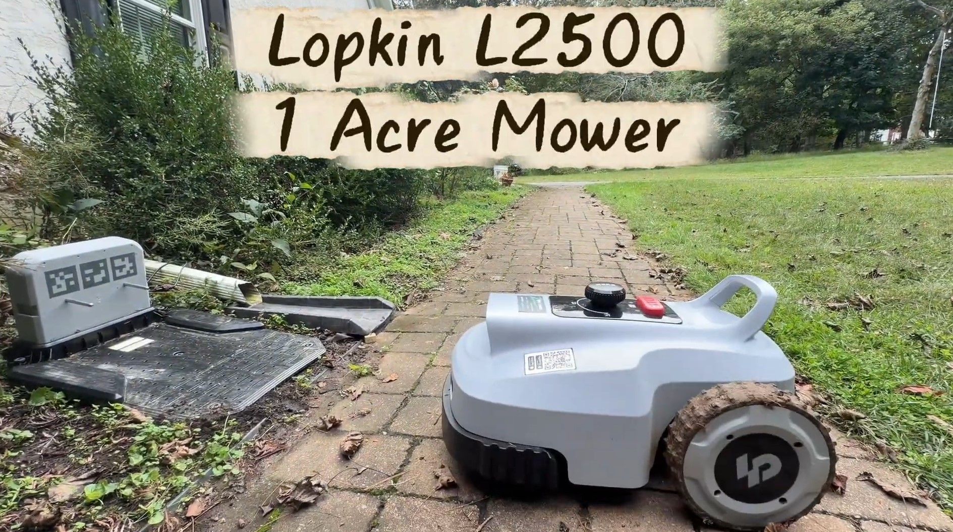 A Lopkin L2500 robot mower on a brick path beside its charging station, next to a one-acre lawn