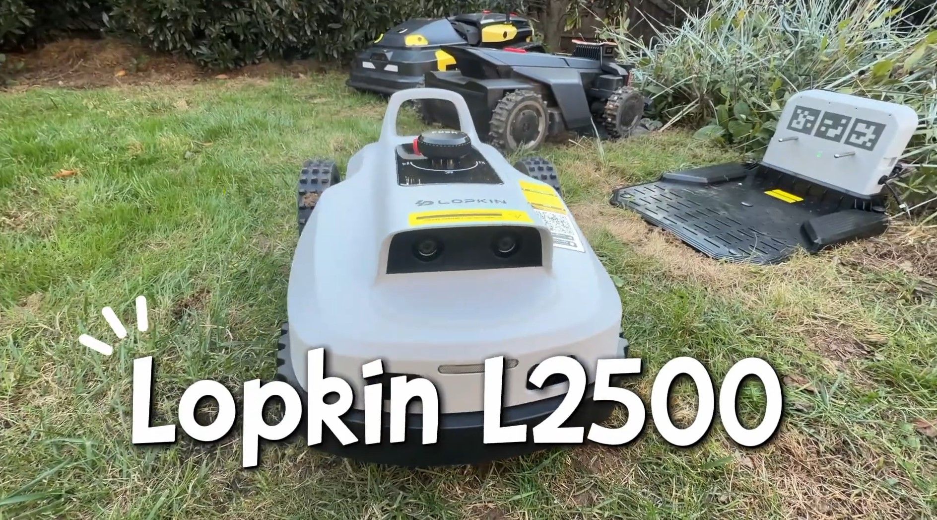 Lopkin L2500 robot mower on a lawn in front of its charging station, with larger robot mowers behind it