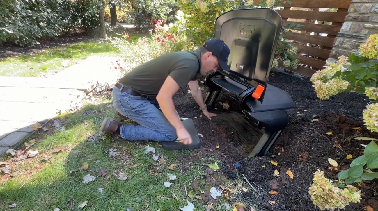 A Zippy Lawnz installer setting a Navimow Garage X over an X430's charging station in a mulch bed in Phoenixville, PA, flip-top roof open