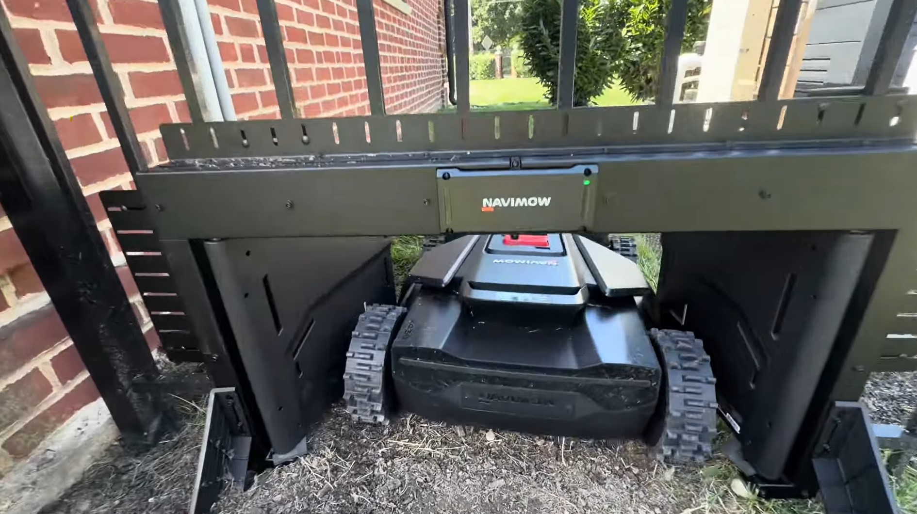 A Navimow MowGate bolted into a black aluminum picket fence, with the cut picket stubs bolted to the gate's top rail