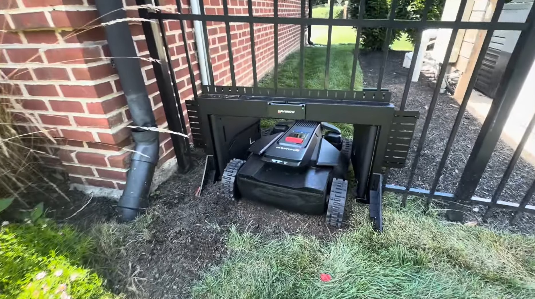 A Segway Navimow MowGate installed in a black aluminum picket fence with a Navimow mower driving through the opening
