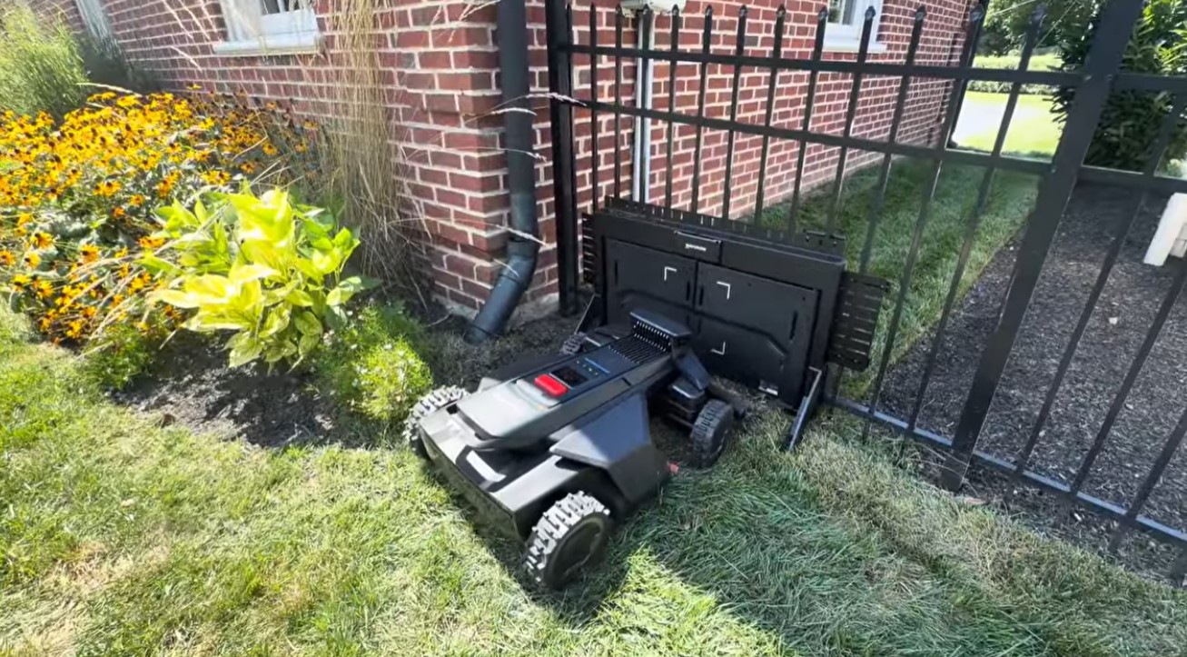 A Navimow robot mower lined up beside a MowGate installed in an aluminum fence next to a flower bed