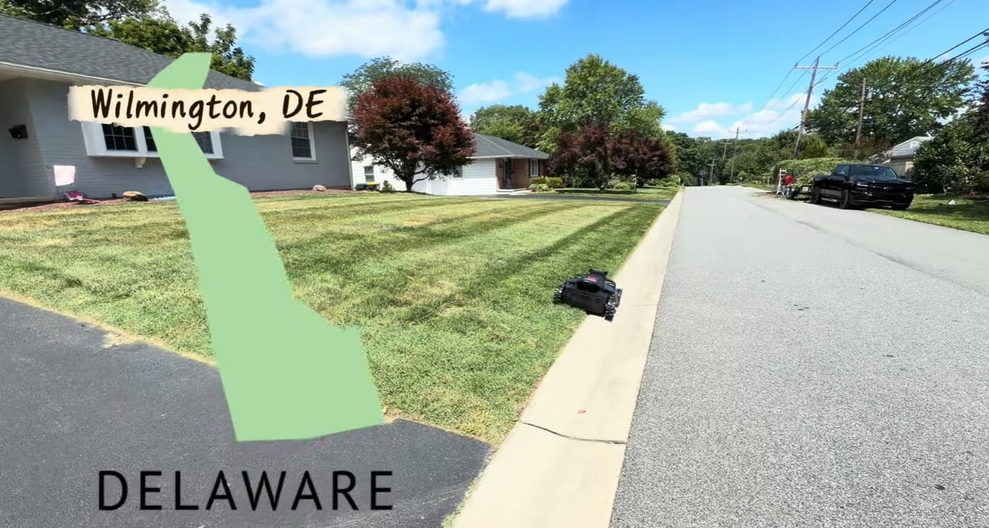 A Segway Navimow X430 robotic mower cutting a striped front lawn in Wilmington, Delaware, with a Delaware state outline overlay