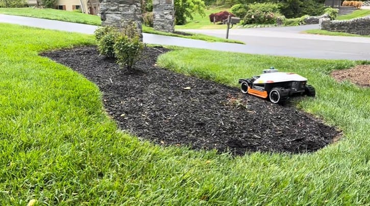 A robot mower navigating cleanly around a mulch bed island in a front yard