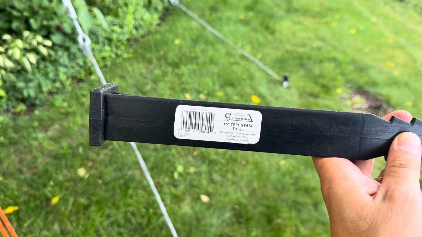 A heavy-duty 15-inch tree stake held in front of tensioned steel cable on the lawn