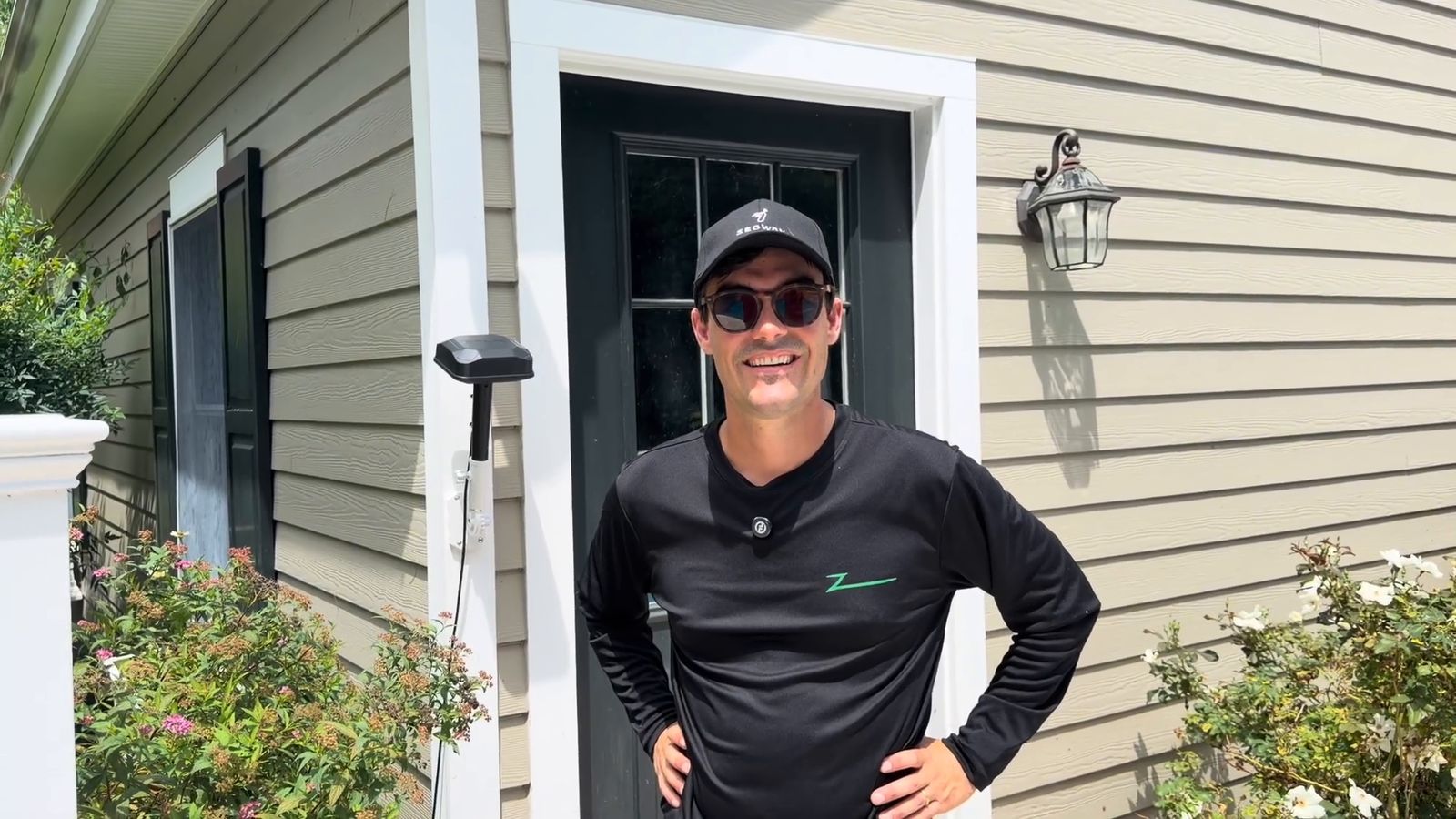 A Zippy Lawnz installer at the customer's front door with the wall-mounted Navimow RTK antenna beside the entry