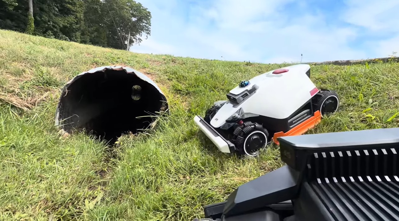 A robot mower field-tested on a steep grassy slope beside a drainage culvert