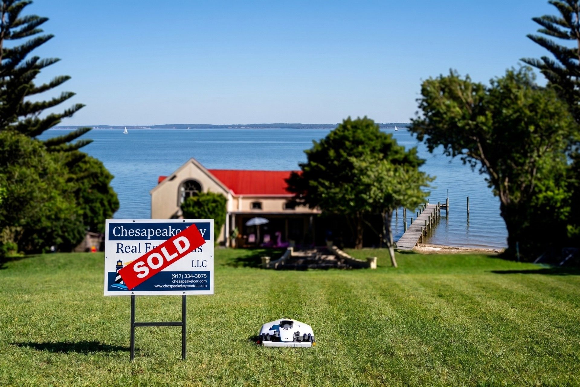 A SOLD real estate sign on a Chesapeake Bay waterfront lawn kept pristine by a robotic mower